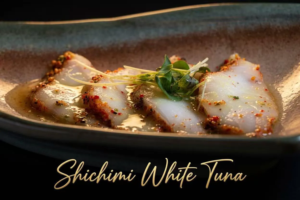Shichimi spiced white tuna carpaccio garnished with microgreens in wide curved glazed ceramic dish with gold text at Akiyo, a Japanese Restaurant in Johnson City